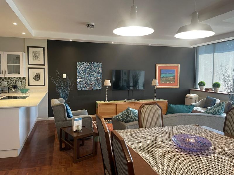 Spacious open-plan living and dining area featuring parquet flooring, modern pendant lighting, and a well-appointed kitchen with stone countertops.
