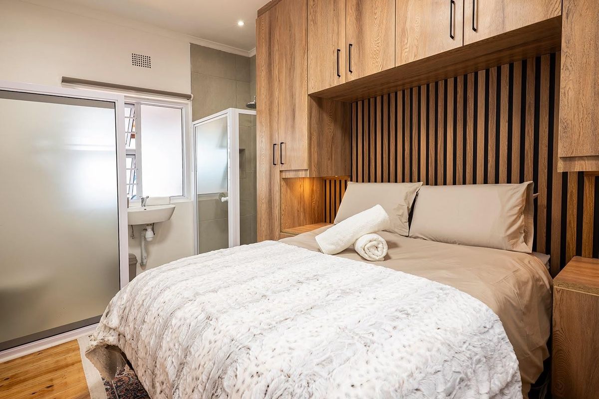 Modern bedroom featuring custom built-in timber cabinetry, a decorative slatted wood headboard, and an integrated en-suite shower and basin area.