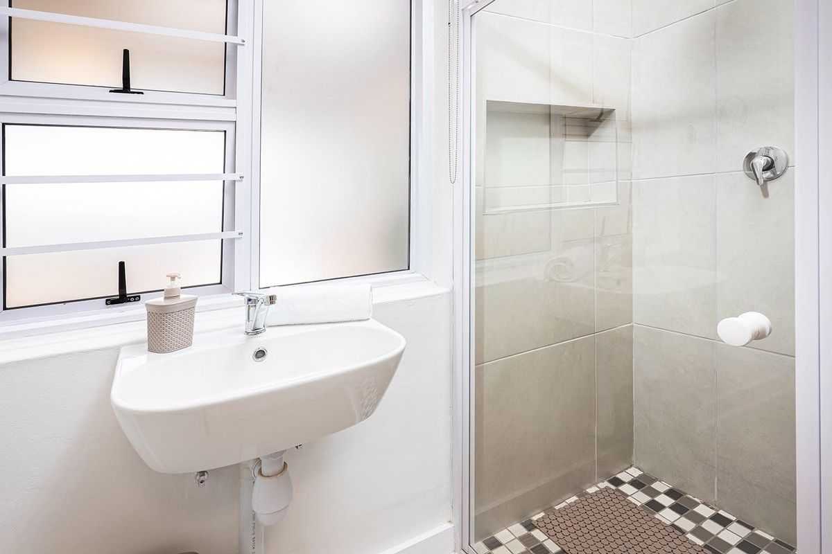 A clean, modern bathroom featuring a wall-mounted basin, a tiled shower enclosure with a built-in niche, and a frosted glass window for privacy.