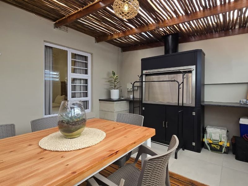 Covered outdoor patio featuring a built-in braai, stone countertop, and rustic thatched roof, ideal for alfresco dining and entertaining.