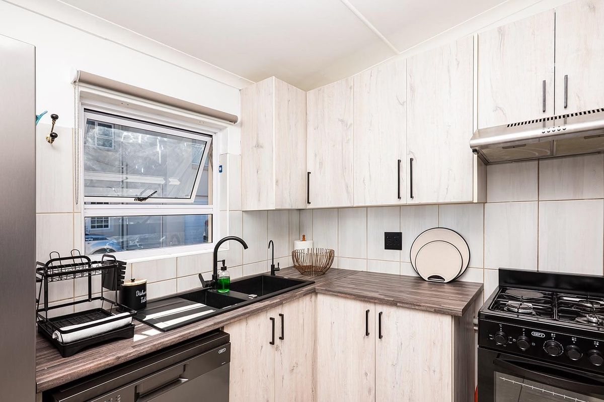 A functional kitchen featuring light wood-look cabinetry, dark countertops, a double sink with modern fixtures, and a built-in extractor fan.