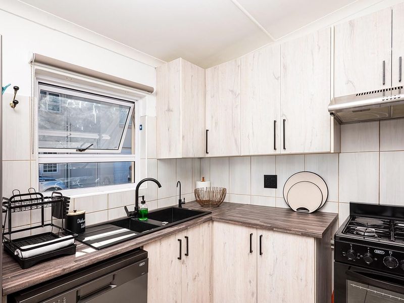 A functional kitchen featuring light wood-look cabinetry, dark countertops, a double sink with modern fixtures, and a built-in extractor fan.