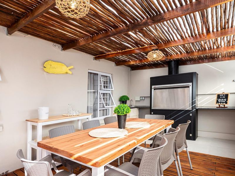 Covered patio area featuring a timber pergola roof, built-in braai, and a functional prep counter with a sink, perfect for outdoor entertaining.