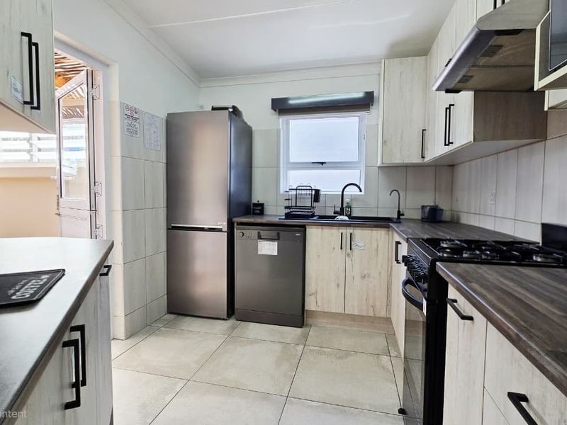 A functional kitchen featuring light wood-grain cabinetry, dark laminate countertops, tiled backsplash, and a gas stove with an integrated extractor fan.
