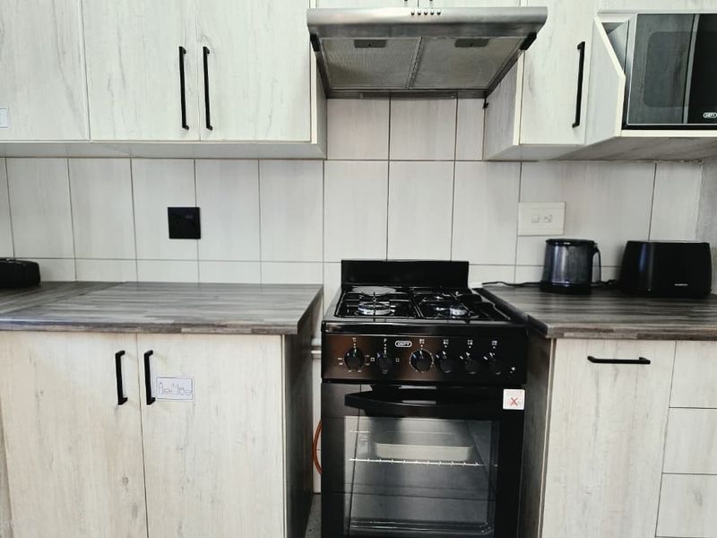 A functional kitchen featuring light wood-grain cabinetry, dark laminate countertops, a gas stove with extractor fan, and a built-in microwave.