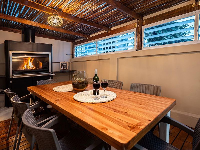Covered outdoor patio featuring a built-in braai, timber pergola ceiling, and timber decking, creating an ideal space for alfresco dining and entertainment.