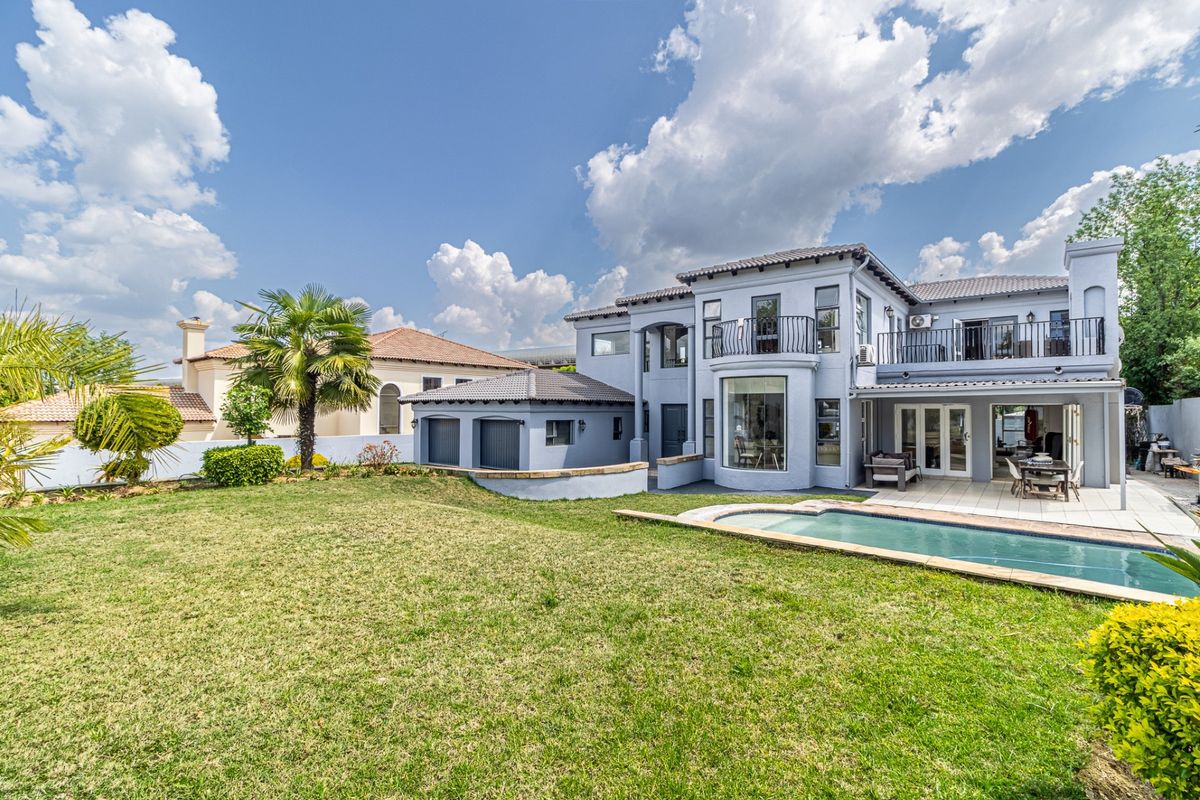 Rear view of a two-story house featuring a swimming pool, tiled patio, upper-level balcony, and a well-maintained garden.