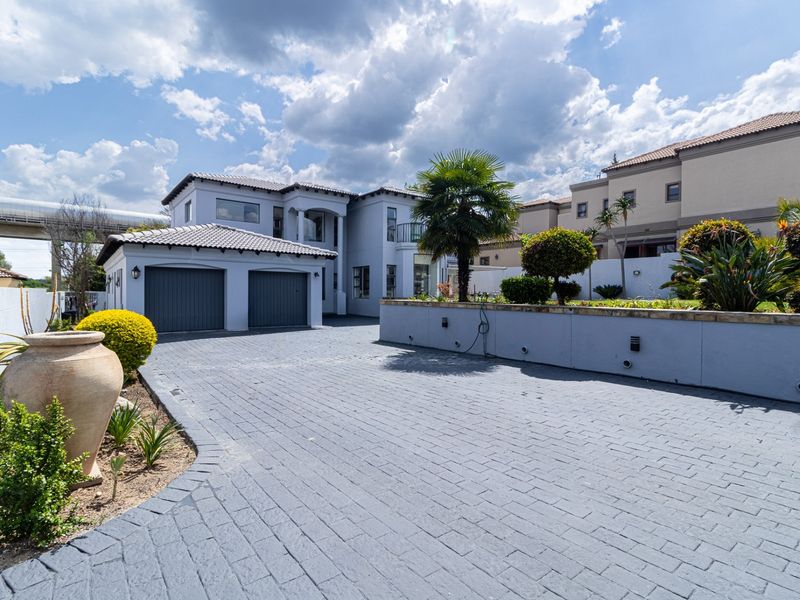 Front view of a modern double-story house featuring a paved driveway, double garage, and landscaped retaining wall.