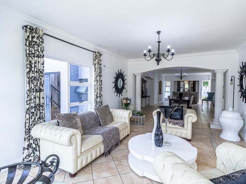 Spacious open-plan living area featuring tiled flooring, decorative columns, and an elegant archway leading to the dining space with a chandelier.