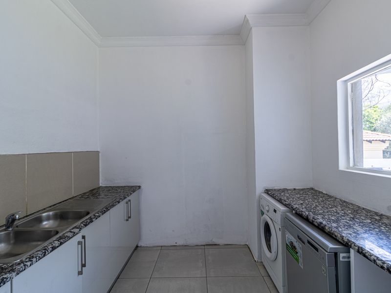 A functional laundry room featuring granite countertops, built-in cabinetry, a double stainless steel sink, and tiled flooring.