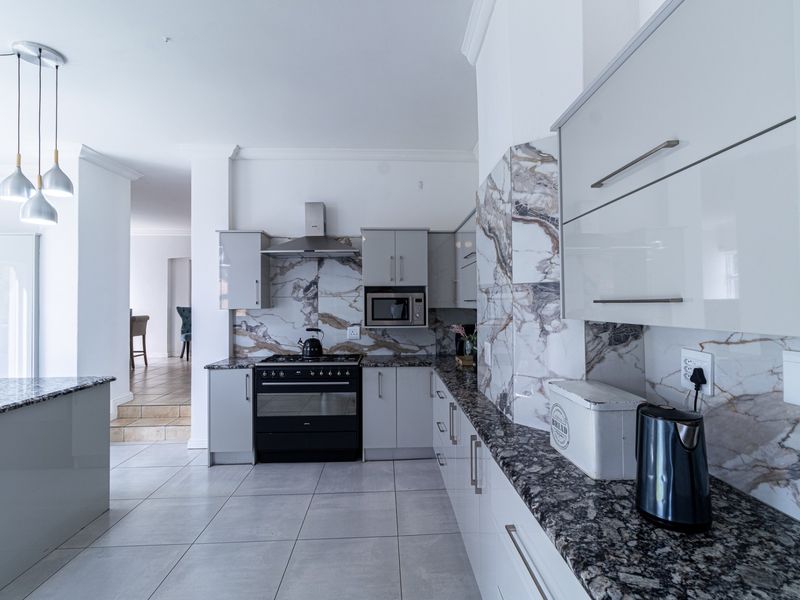 Modern kitchen featuring high-gloss cabinetry, granite countertops, marble-look splashbacks, and integrated appliances, flowing into an adjacent living area.