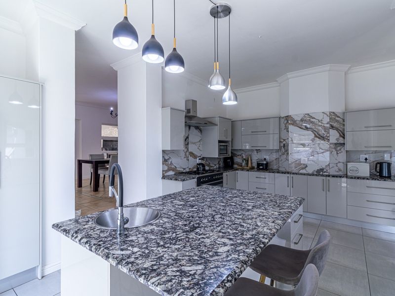 Modern kitchen featuring a central island with granite countertops, high-gloss cabinetry, marble-look splashbacks, and contemporary pendant lighting.