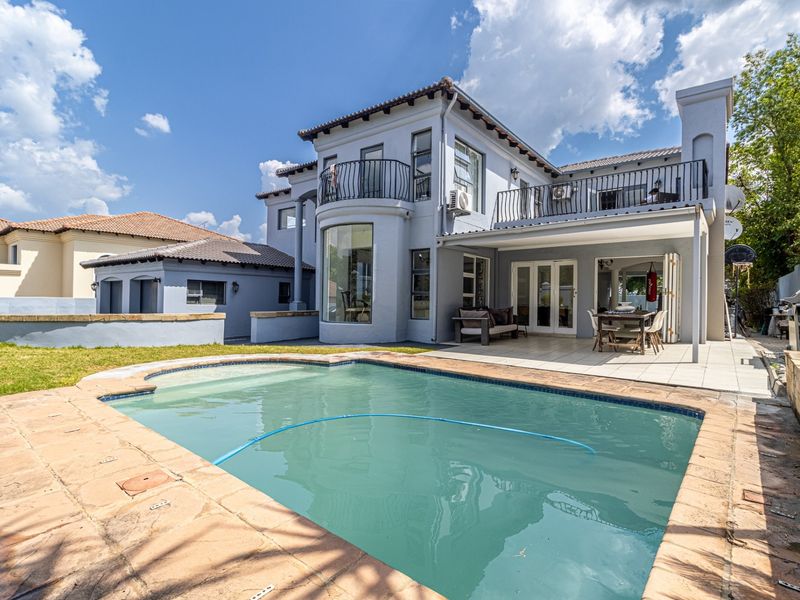 Rear view of a two-story residence featuring a swimming pool, covered patio, and upper-level balconies with wrought iron railings.