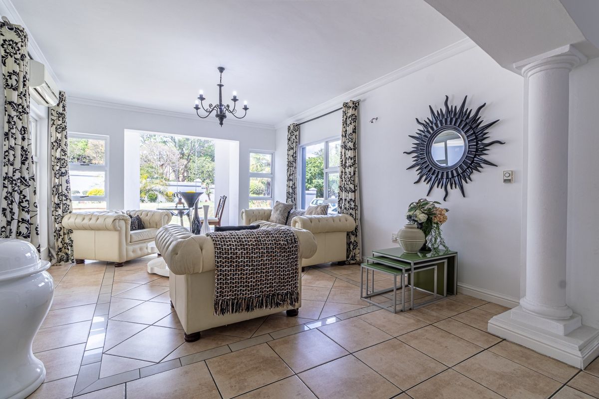 Spacious living room featuring tiled flooring, a decorative column, and large windows providing natural light and garden views.