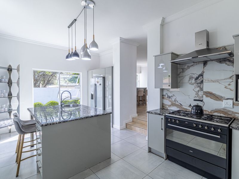 Modern kitchen featuring a central island with granite countertops, gas stove, integrated extractor fan, and elegant marble-look splashback with tiled flooring.