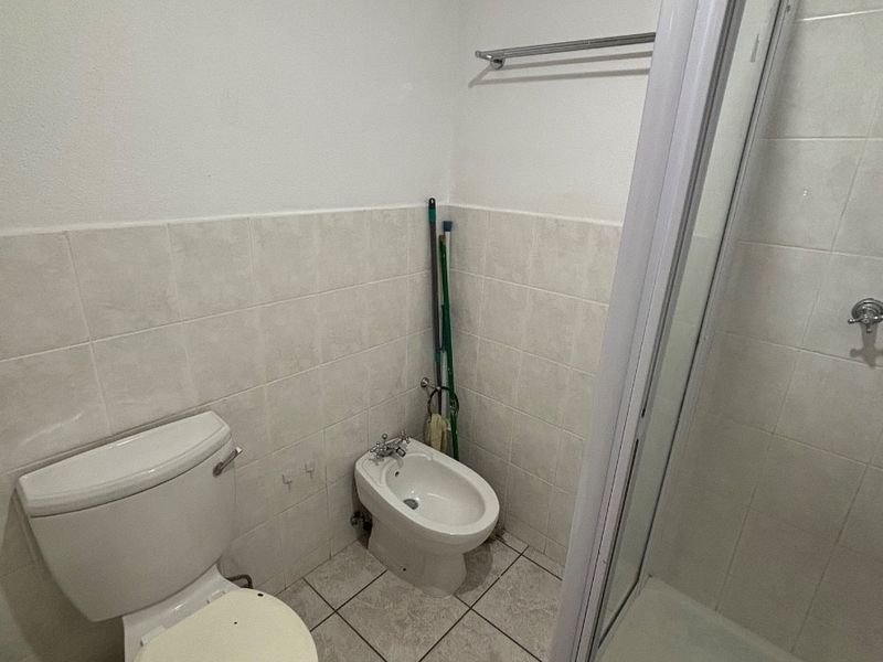 A functional bathroom featuring a shower enclosure, toilet, and bidet with neutral wall and floor tiling.