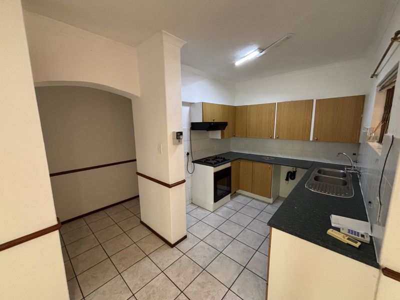 A functional kitchen featuring built-in cabinetry, gas hob, oven, and double sink, with tiled flooring and an adjacent open-plan transition area.