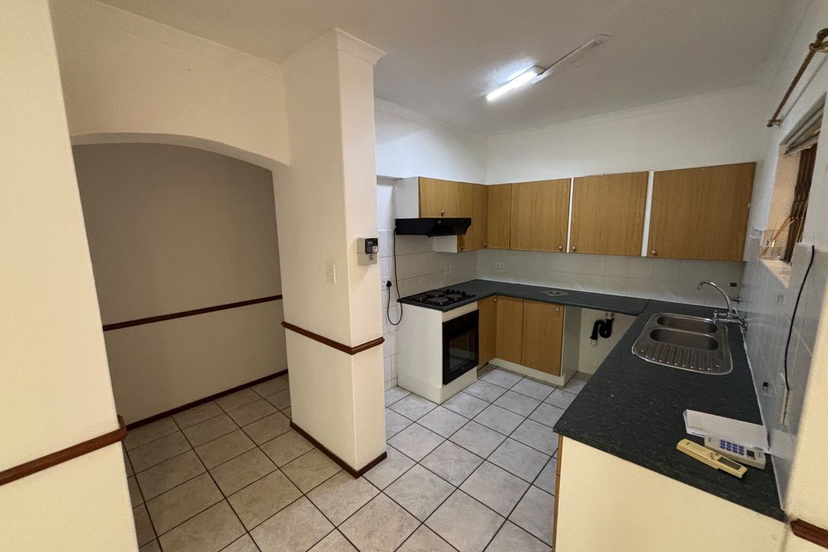 A functional kitchen featuring built-in cabinetry, gas hob, oven, and double sink, with tiled flooring and an adjacent open-plan transition area.