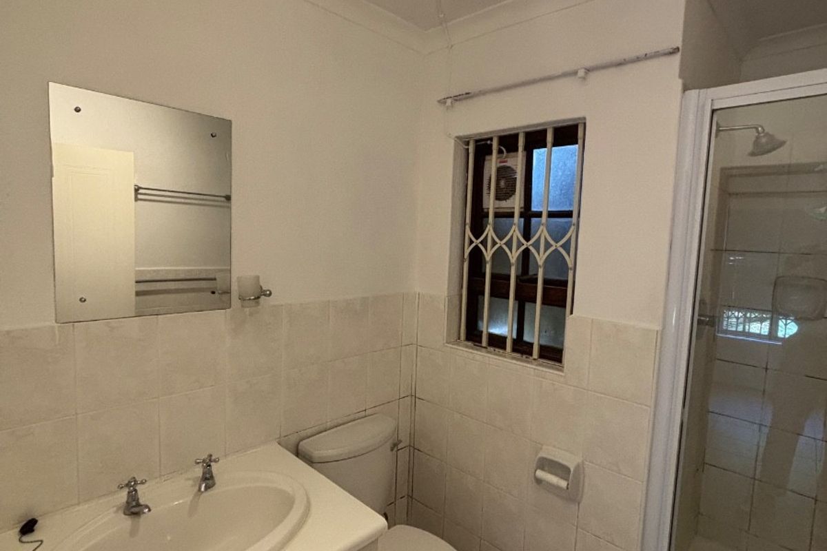 A functional bathroom featuring a vanity cabinet, toilet, and a separate shower enclosure with tiled finishes and a security-gated window.
