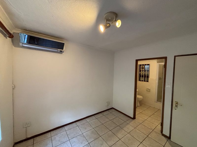 A clean, empty bedroom featuring tiled flooring, an integrated air conditioning unit, and direct access to an en-suite bathroom.