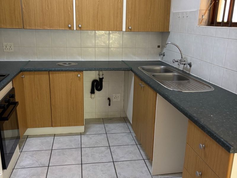 A functional kitchen featuring laminate cabinetry, dark countertops, a double stainless steel sink, and tiled flooring, with space provided for an under-counter appliance.