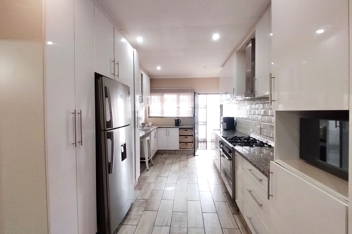 Modern galley-style kitchen featuring high-gloss white cabinetry, granite countertops, a gas hob with extractor, and stylish subway tile backsplash.