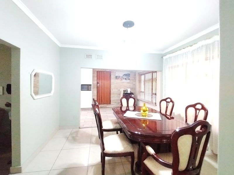 A dining room featuring tiled flooring, coved ceilings, and venetian blinds, with an open transition to an adjacent kitchen area.