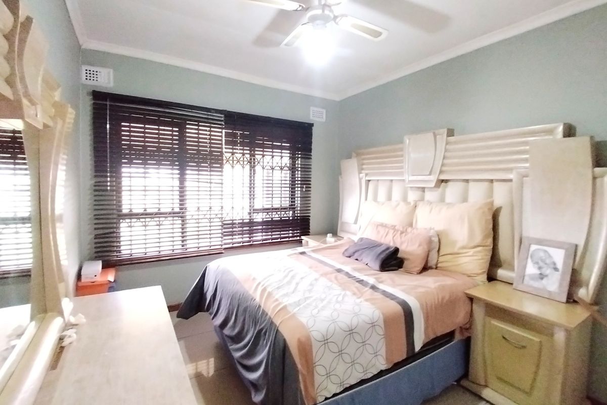 A well-lit bedroom featuring tiled flooring, a ceiling fan, and security gates on the windows, providing a functional and comfortable sleeping space.