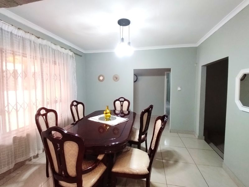 A well-maintained dining room featuring neutral wall tones, tiled flooring, and a central pendant light fixture, providing a functional space for family meals.