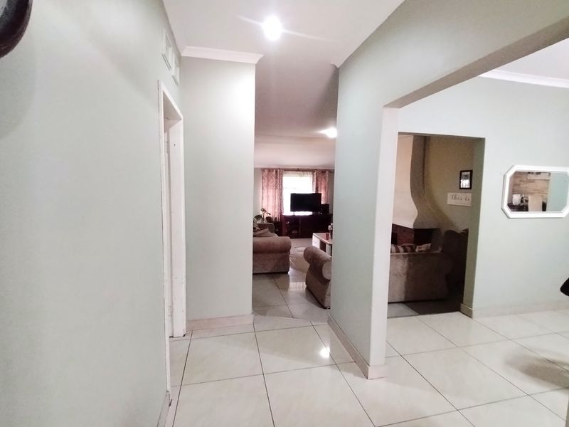 A bright hallway with neutral tiled flooring and coved ceilings, providing an open transition into the adjacent living area with a built-in fireplace.
