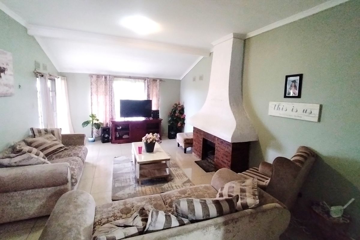 A spacious living room featuring a prominent brick fireplace, vaulted ceilings, and neutral tiled flooring, offering a comfortable and inviting atmosphere.