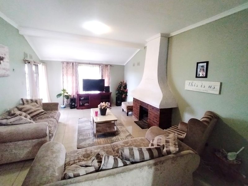 A spacious living room featuring a prominent brick fireplace, vaulted ceilings, and neutral tiled flooring, offering a comfortable and inviting atmosphere.