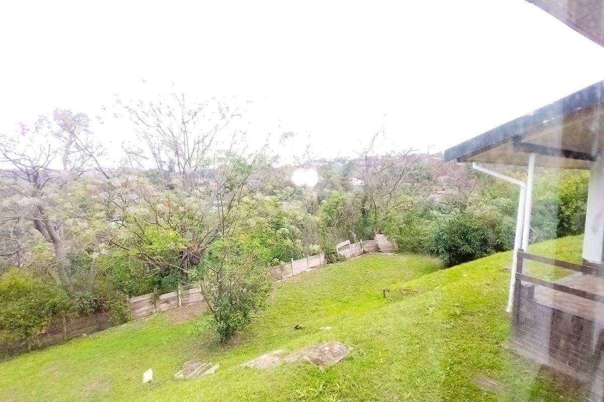A view of the rear garden area featuring a sloped lawn and perimeter fencing, captured from an elevated position.