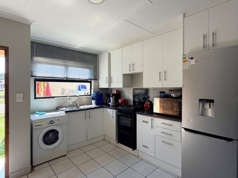 A functional kitchen featuring white cabinetry, tiled flooring, a stainless steel sink, and space for a washing machine and freestanding stove.