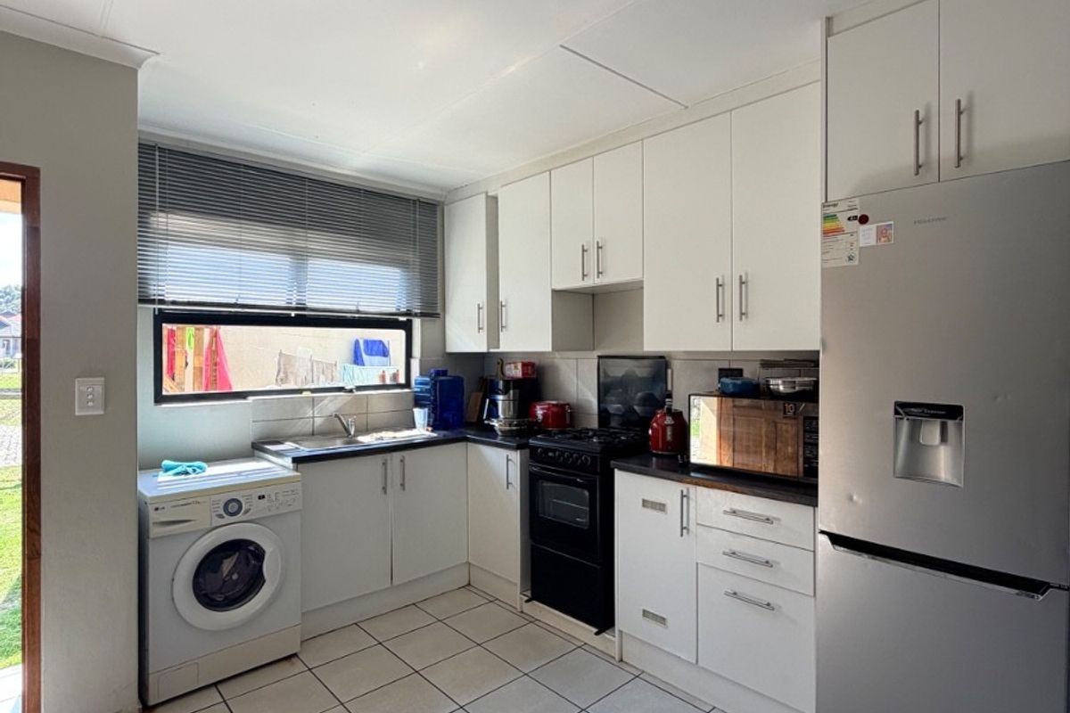 A functional kitchen featuring white cabinetry, tiled flooring, a stainless steel sink, and space for a washing machine and freestanding stove.
