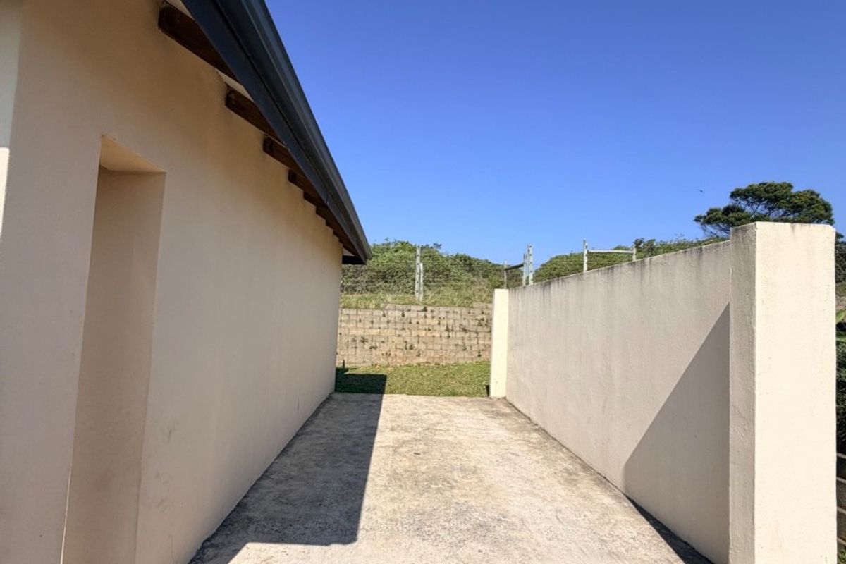 A side exterior area featuring concrete paving, a boundary wall, and a retaining wall, showing signs of weathering and maintenance requirements.