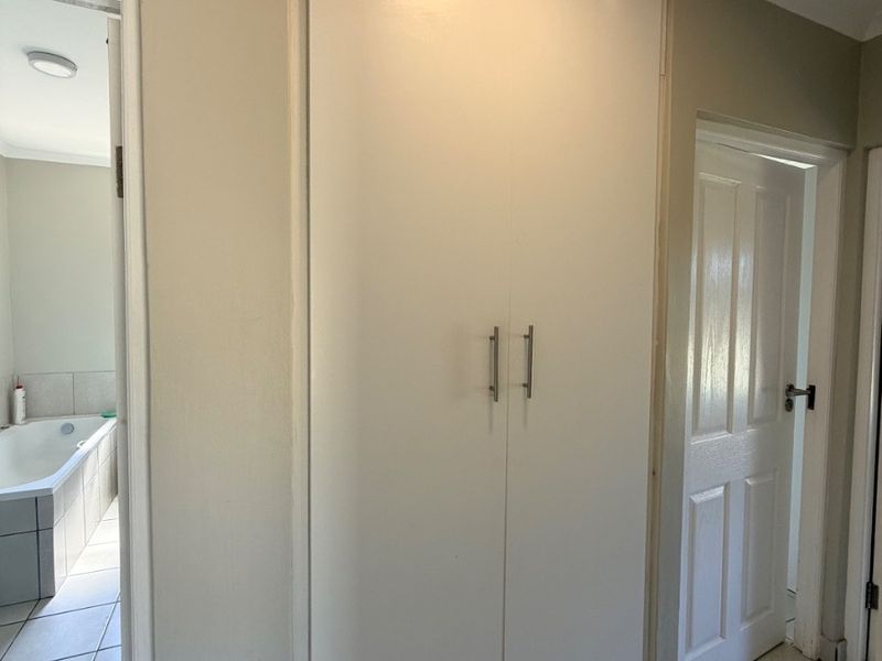 A clean hallway featuring tiled flooring and a large built-in linen cupboard, providing convenient storage space between rooms.