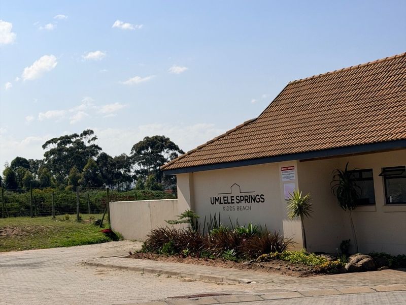 Front exterior view of the Umlele Springs property entrance, featuring a paved driveway, boundary wall, and tiled roof structure.