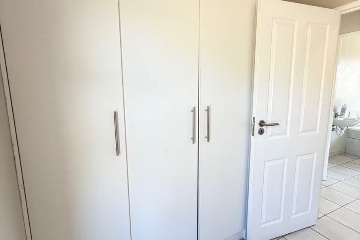 A bedroom featuring built-in white cupboards, tiled flooring, and a coved ceiling, with an adjacent view into a bathroom.