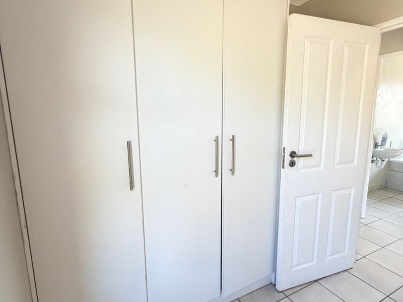 A bedroom featuring built-in white cupboards, tiled flooring, and a coved ceiling, with an adjacent view into a bathroom.
