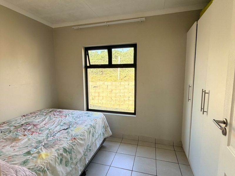 A functional bedroom featuring tiled flooring, built-in cupboards, and an aluminium-framed window providing natural light.