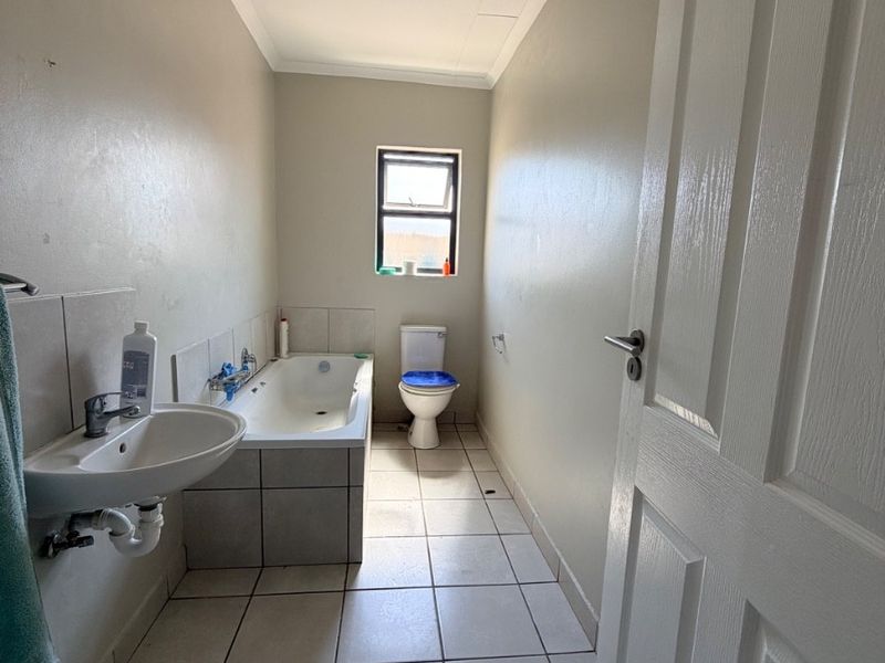 A functional bathroom featuring a pedestal basin, built-in bathtub, and toilet with neutral tiled flooring and splashbacks.