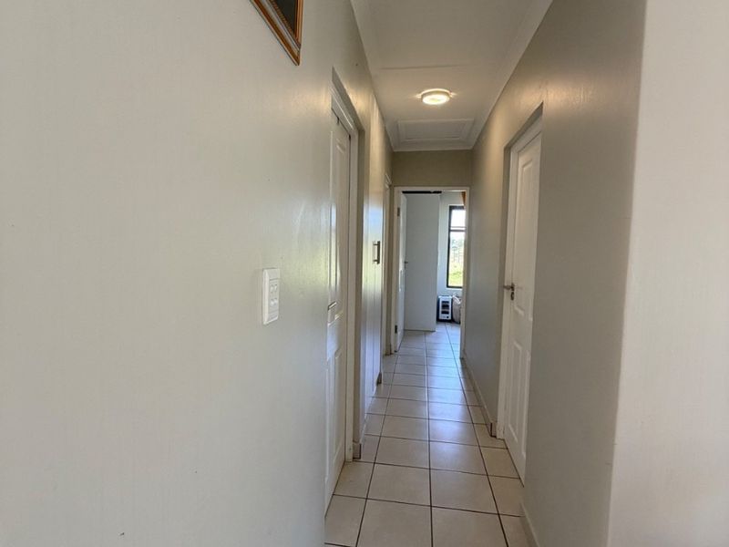 A clean, neutral-toned hallway featuring tiled flooring, cove cornicing, and multiple internal doors leading to adjacent rooms.