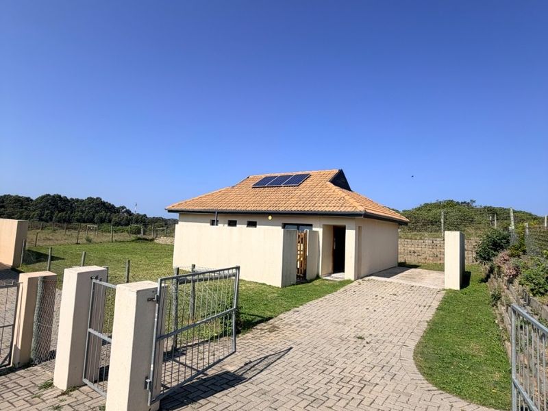 Front view of the property featuring a paved driveway, boundary wall with metal gate, and a tiled roof equipped with solar panels.
