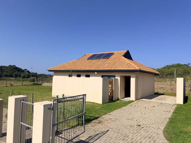A detached residential building featuring a tiled roof with installed solar panels, a paved driveway, and a secure gated entrance.
