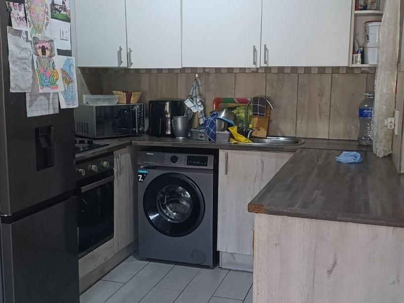 Compact kitchen featuring modern wood-look cabinetry, laminate countertops, integrated oven and hob, and a tiled backsplash, providing a functional workspace.