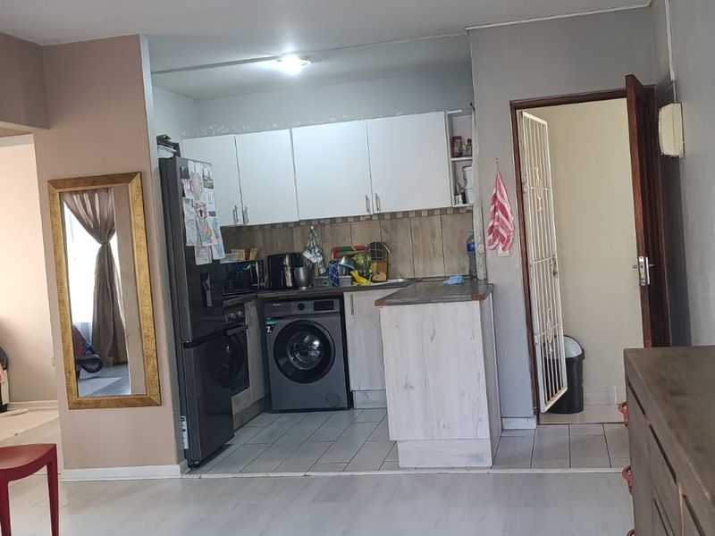 Open-plan living area featuring a compact kitchen with built-in cabinetry, tiled floors, and direct access to a secondary room through a security gate.