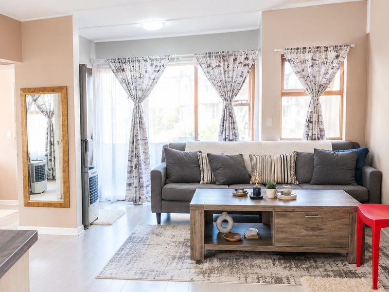 A bright and well-maintained living room featuring laminate flooring and large windows that provide ample natural light.