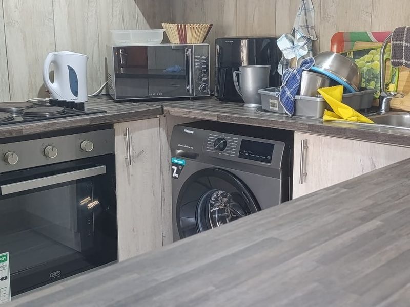 Compact kitchen featuring laminate countertops, built-in oven, electric hob, stainless steel sink, and integrated washing machine with wood-look wall paneling.
