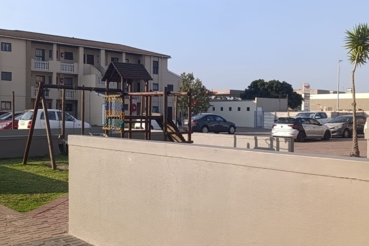 Communal outdoor area featuring brick paving, a built-in braai, and playground equipment within an apartment complex setting.
